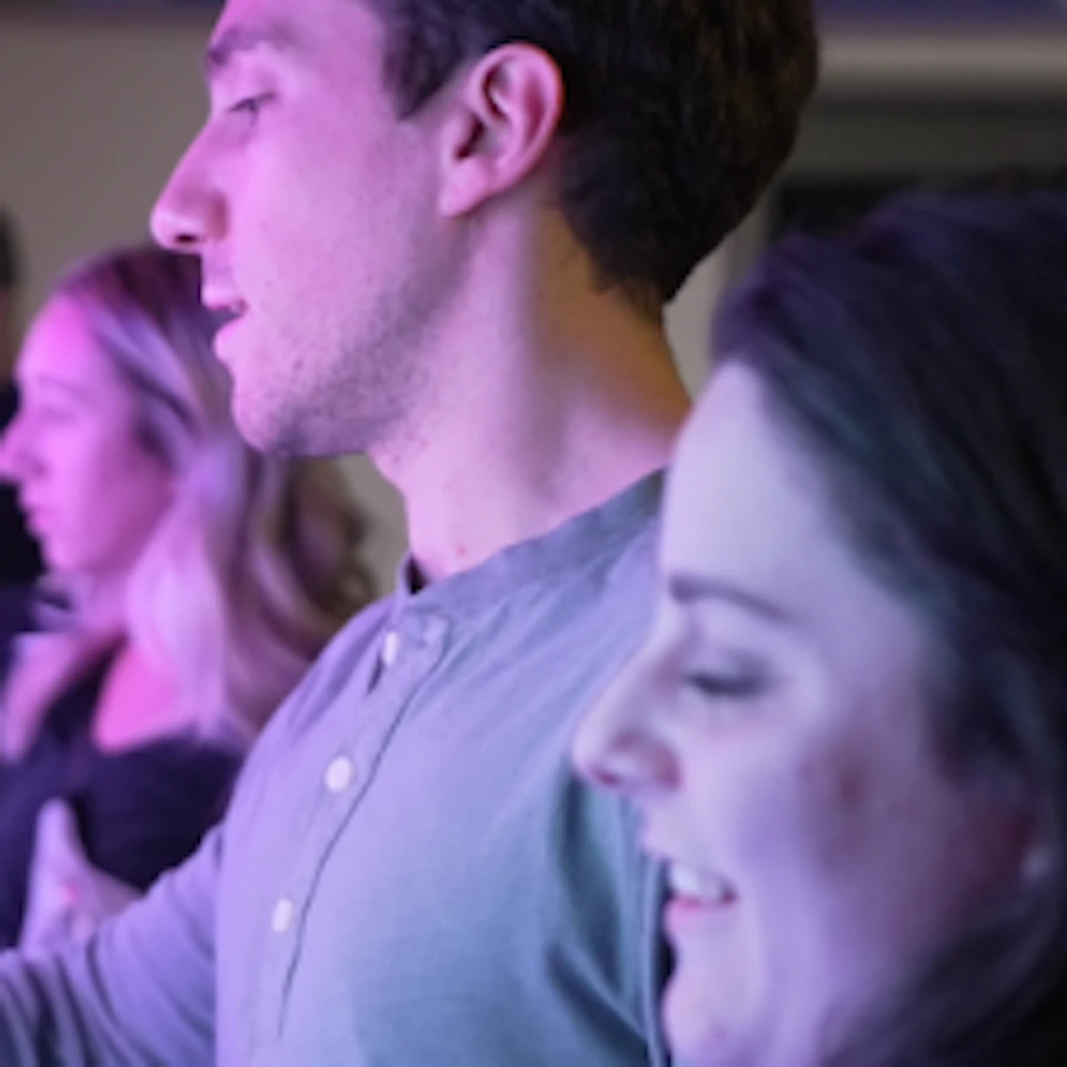 People interact with a wall of colorful, illuminated buttons in a dimly lit room.