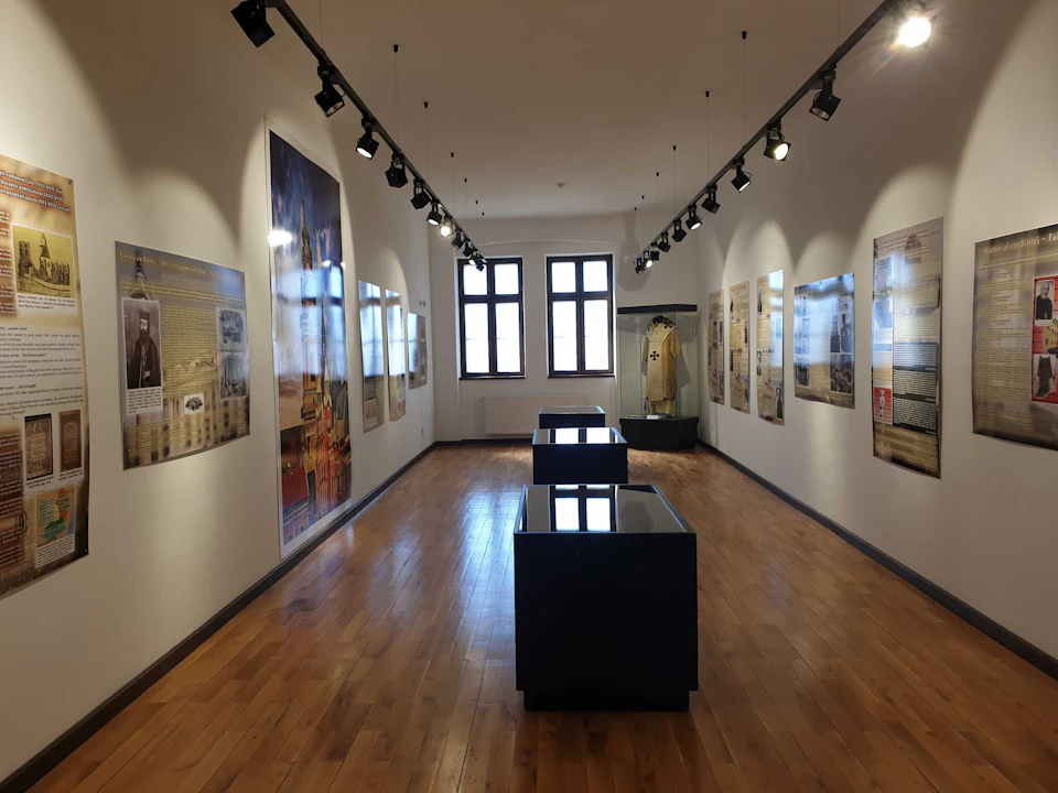 A gallery with wooden floors, informational panels on the walls, display cases, and a lit exhibit under ceiling track lights.