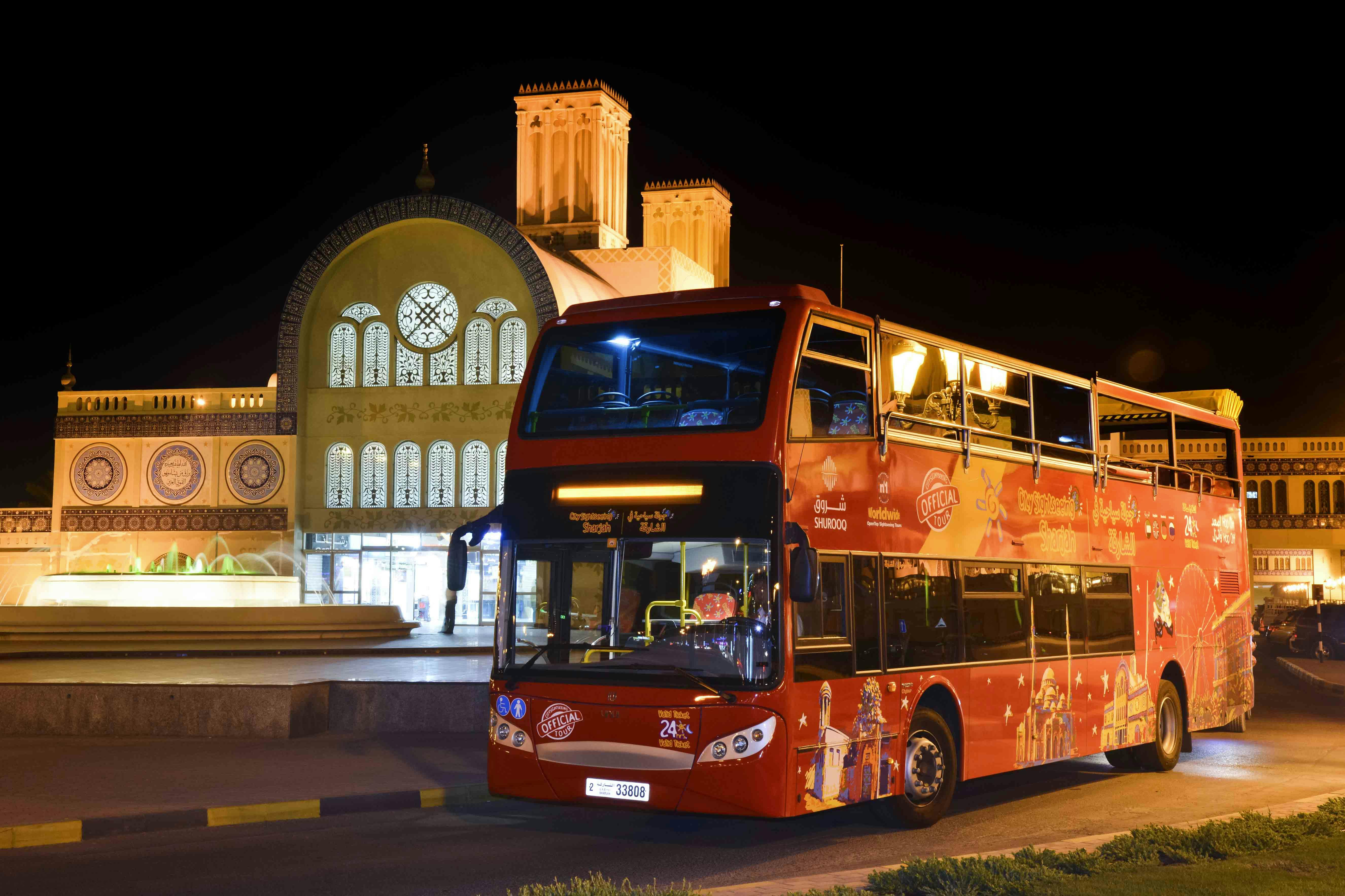 A red double-decker tour bus is parked in front of an illuminated traditional building at night.