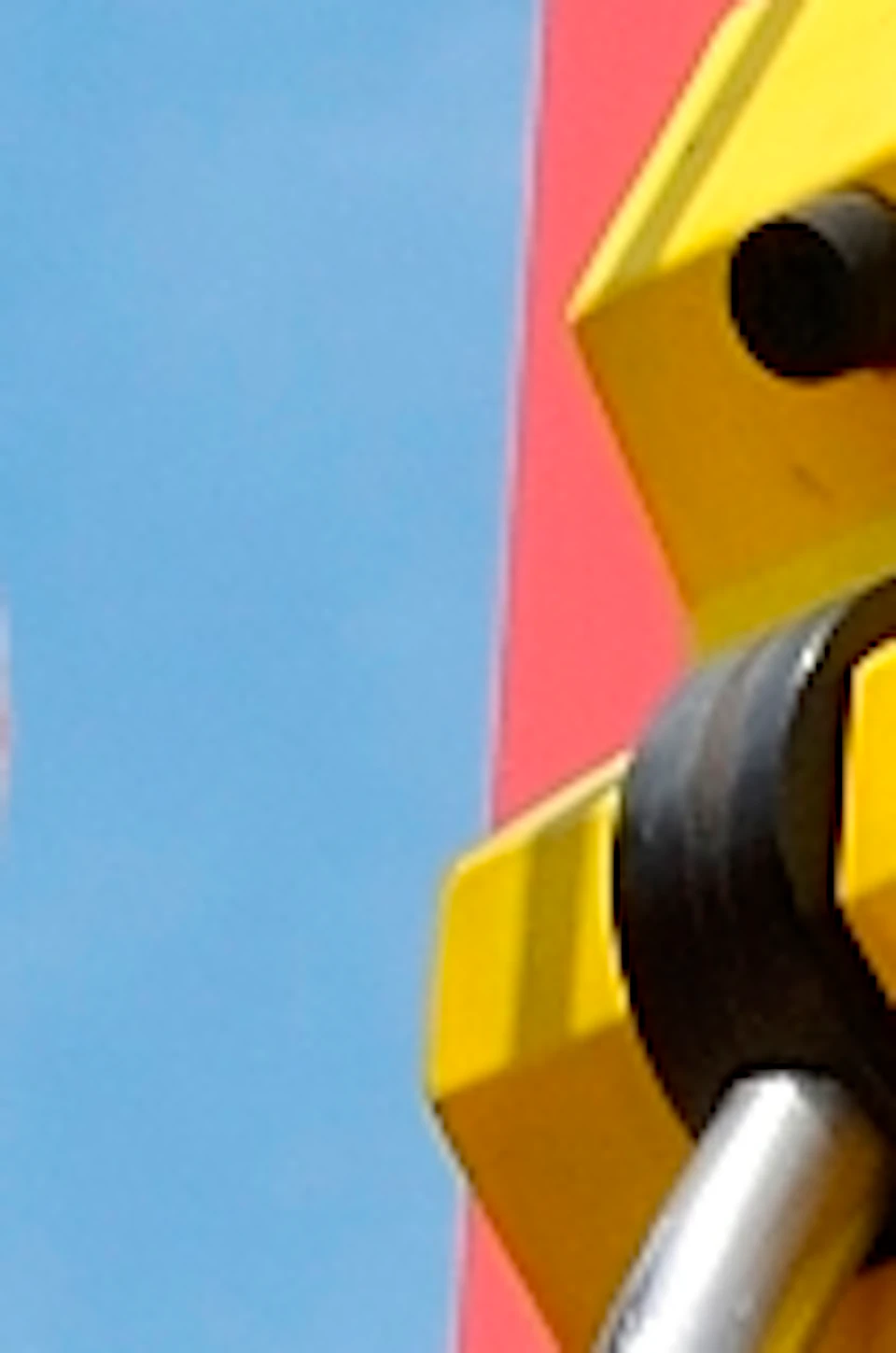 Two children smiling on a swing seat ascending a colorful vertical ride against a clear blue sky. Trees are visible in the background.