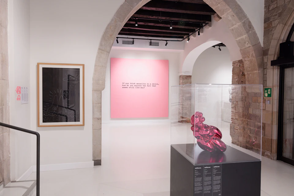 A modern art gallery with a pink text artwork, a framed piece, and a red sculpture in a glass case on display.