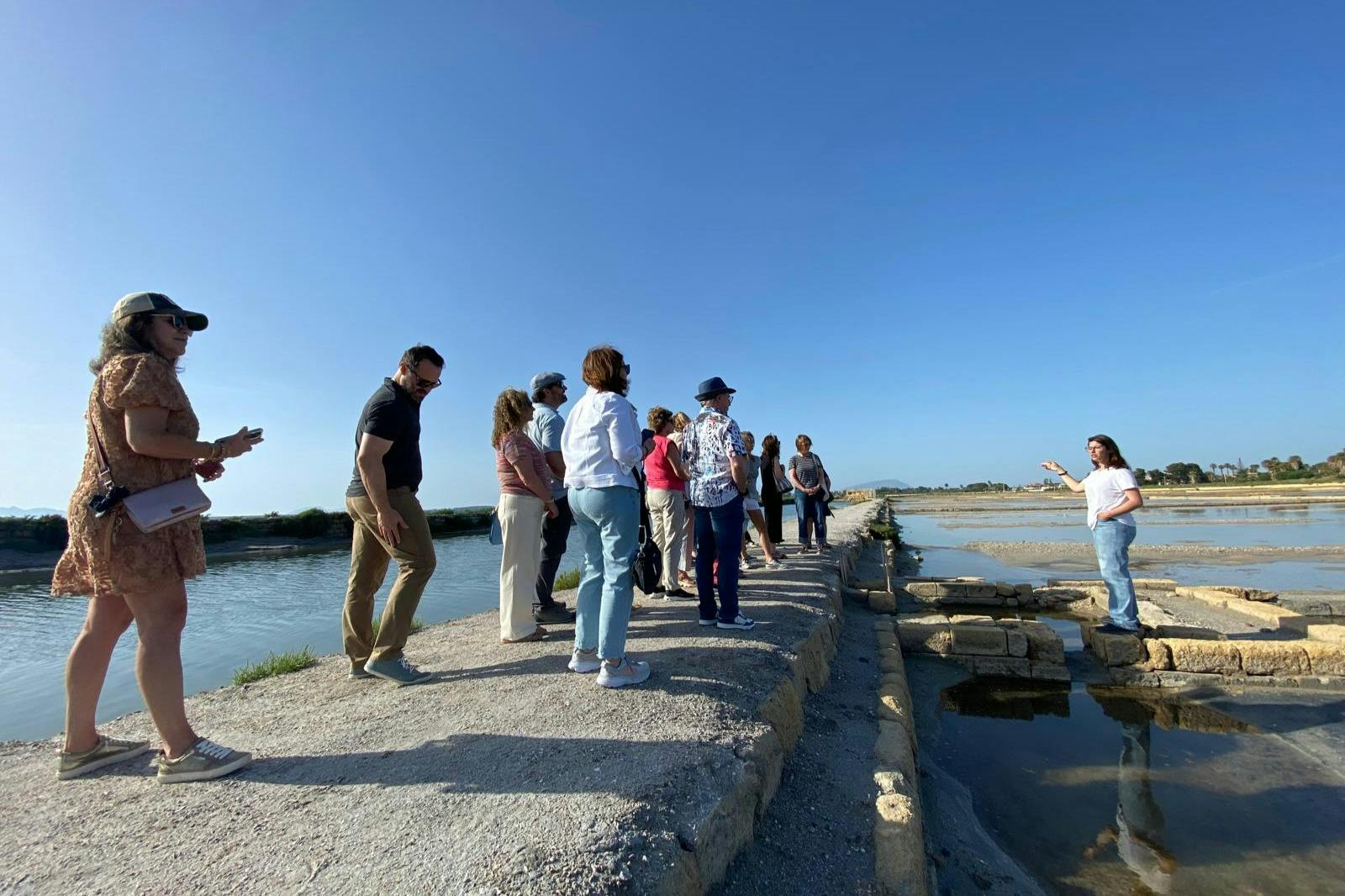 A group of people standing on a narrow path near a water channel under a clear blue sky.