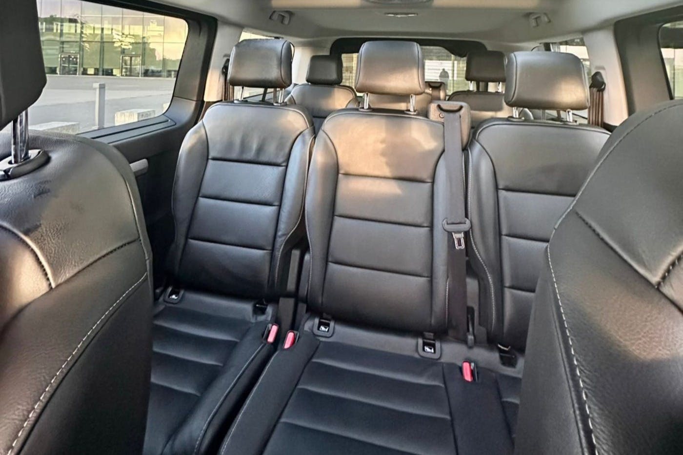 Interior of a vehicle showing three rows of black leather seats, with sunlight coming through the windows.