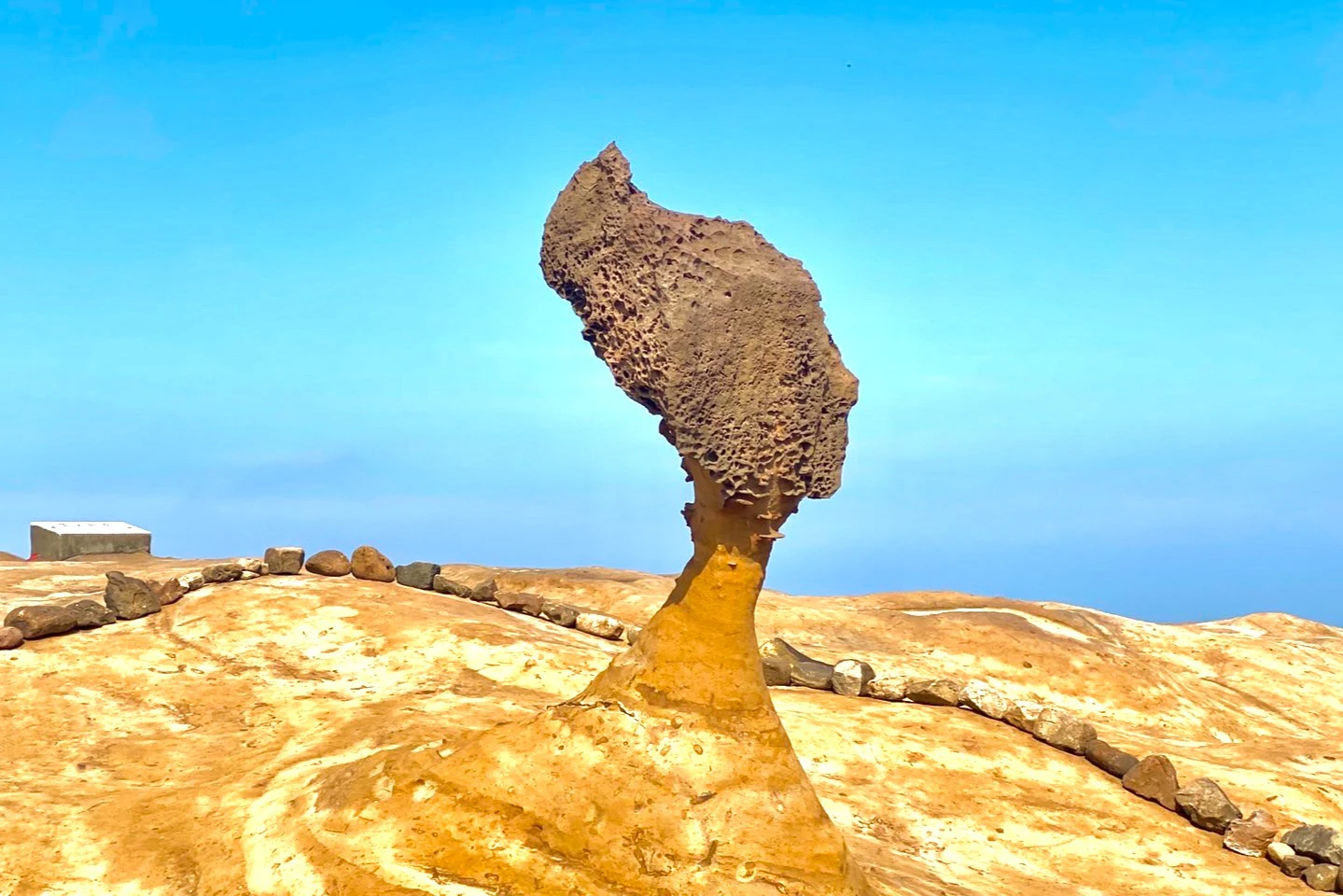 A mushroom-shaped rock formation stands in a barren, sandy landscape against a clear blue sky.