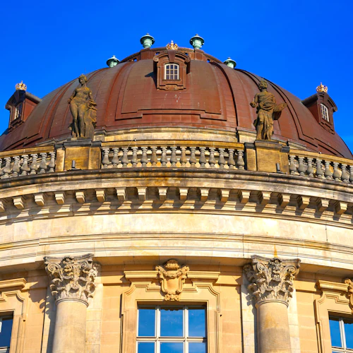 Kupol i barockstil med statyer och dekorativa element mot en klarblå himmel. Strukturen har utsmyckade pelare och en balustrad.
