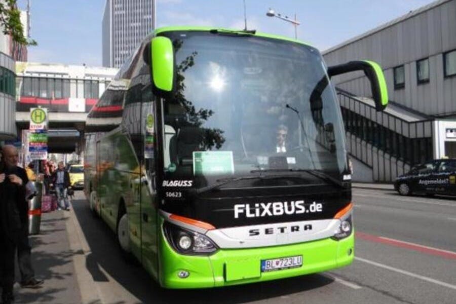 Ένα πράσινο και μαύρο FlixBus σταθμευμένο σε έναν δρόμο σε μια πόλη με κτίρια στο παρασκήνιο.