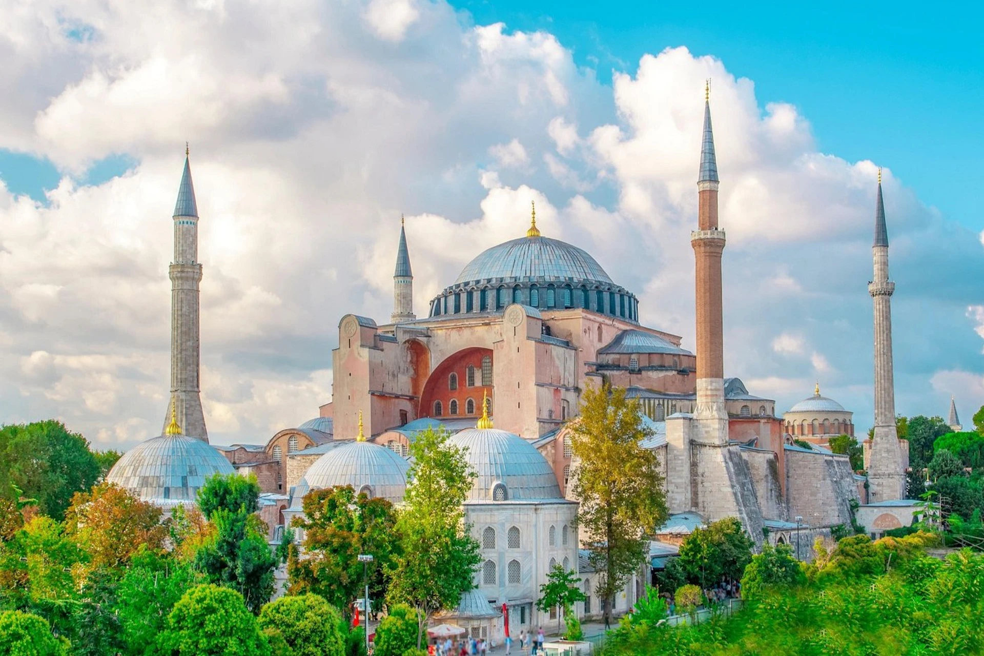 A historic building with a large dome and four minarets surrounded by trees under a partly cloudy sky.