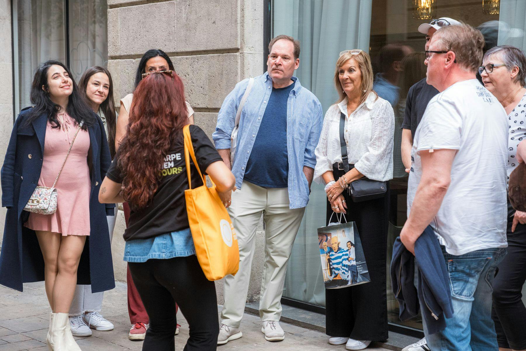 Um grupo de pessoas de pé e a conversar no exterior de um edifício com uma janela de vidro. Uma pessoa segura um saco de compras.