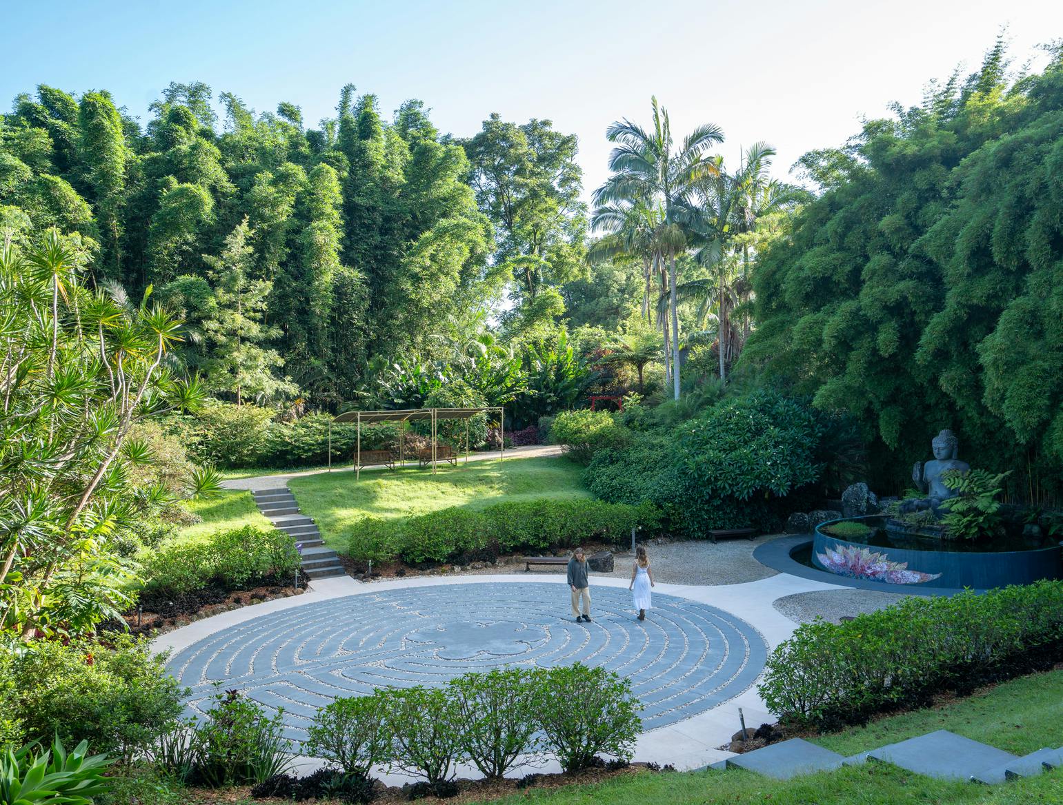豊かな緑と木々に囲まれた庭園の螺旋状の小道を歩いている2人の人物。
