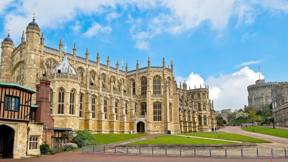 Gothic-style building with ornate spires and large windows, surrounded by green lawns under a blue sky with some clouds.
