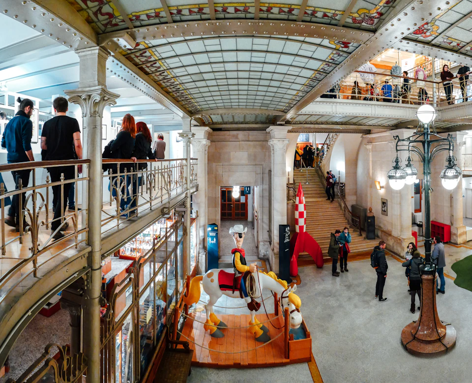People inside a two-story building with ornate railings and a decorative ceiling. A carousel horse and other decorations are visible.