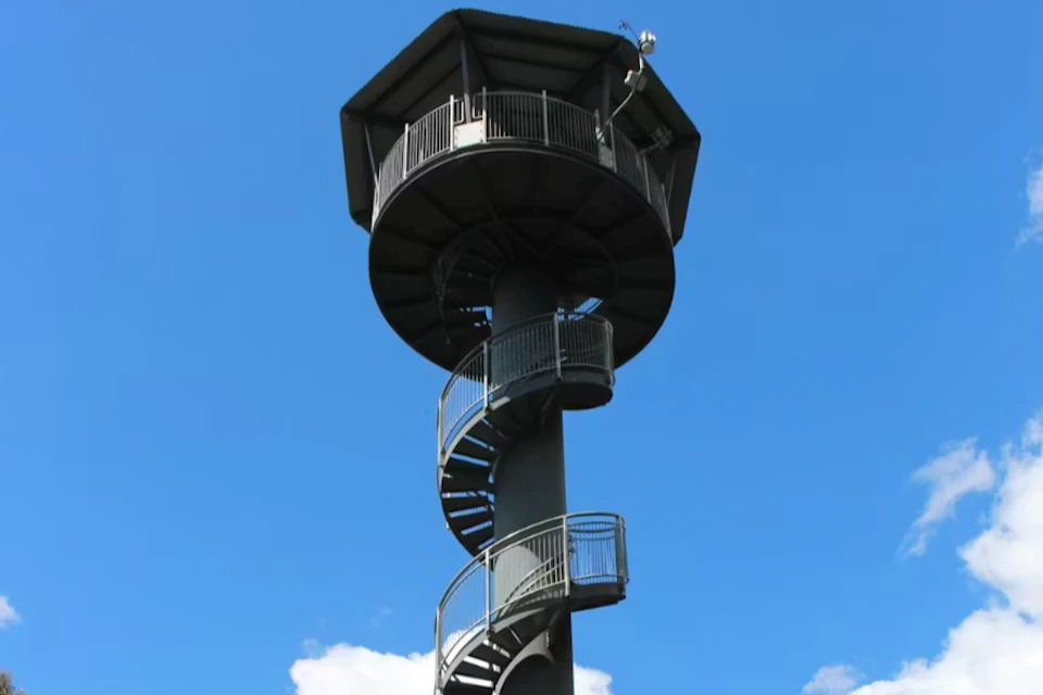 A tall observation tower with a spiral staircase and a hexagonal viewing platform against a clear blue sky.