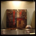 Abstract painting with dark colors and red streaks on a display wall; a soccer ball rests on a glass shelf below.