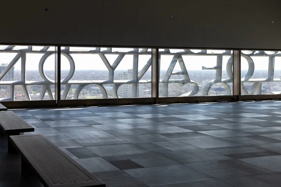 Interior view of a modern building with large windows featuring decorative text and a cityscape in the background.
