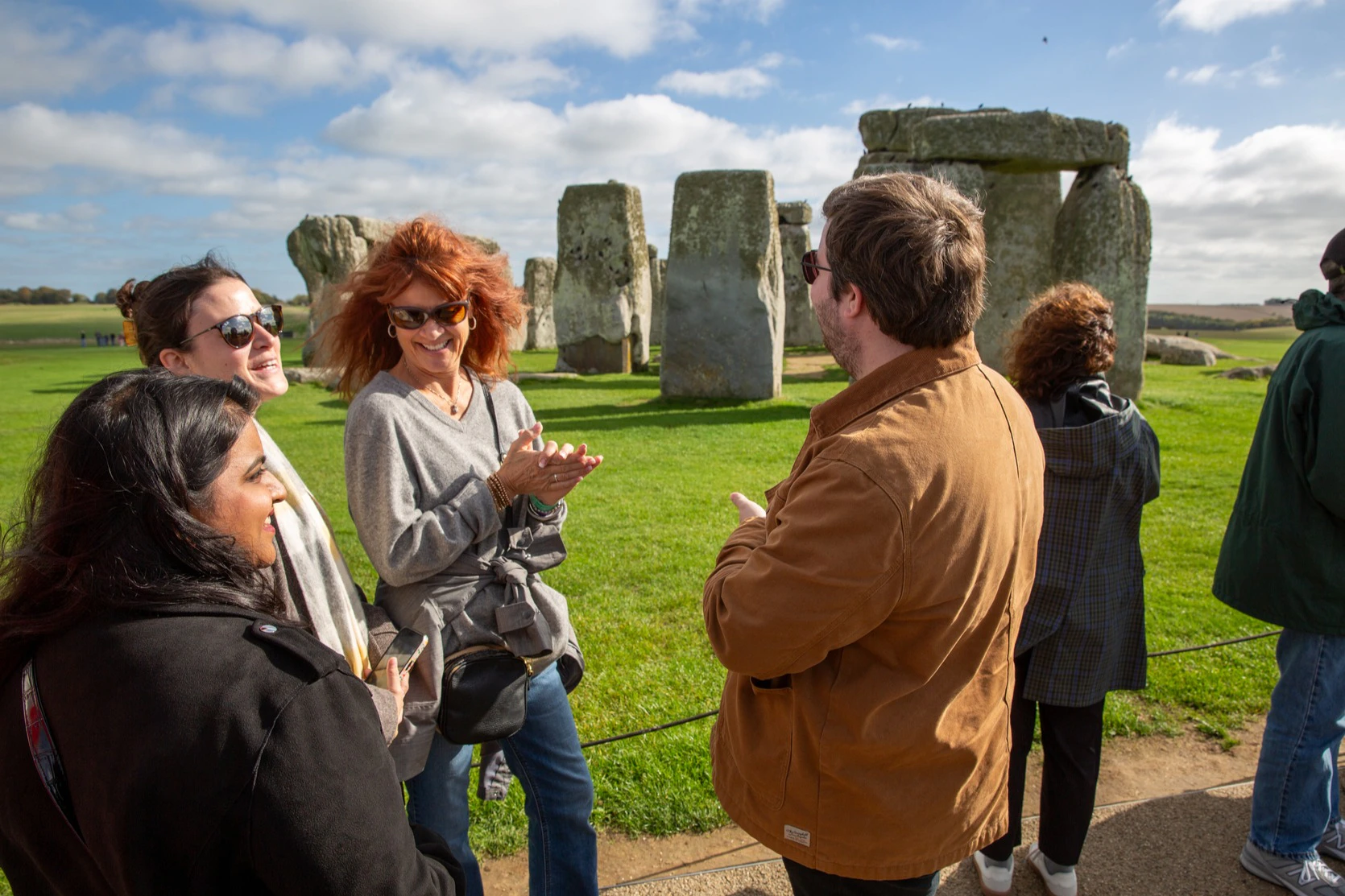 A group of people talking and smiling outdoors near Stonehenge on a sunny day.