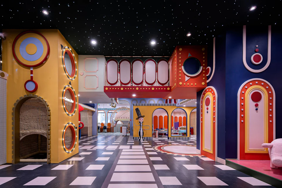 A colorful indoor space with playful, whimsical architecture, featuring starry black ceilings and vibrant geometric decor.