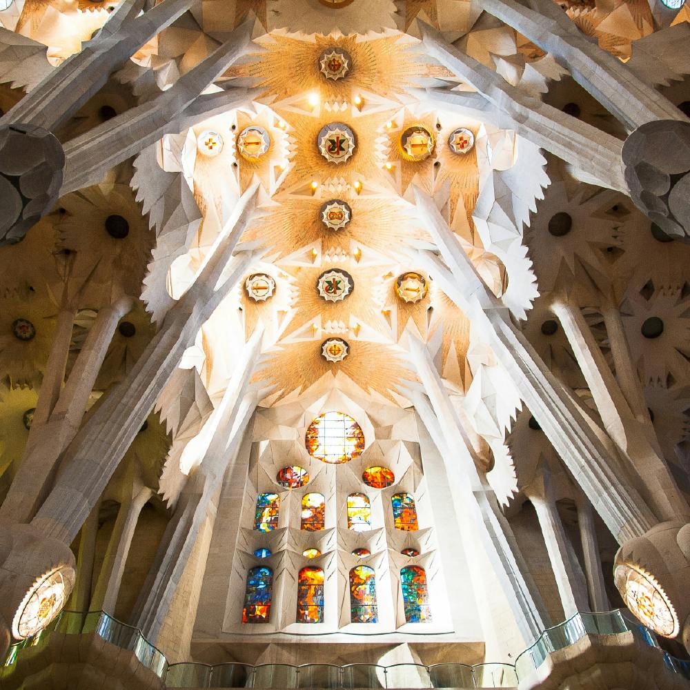 Plafond de cathédrale complexe avec des motifs géométriques, des colonnes et des vitraux colorés représentant diverses scènes.