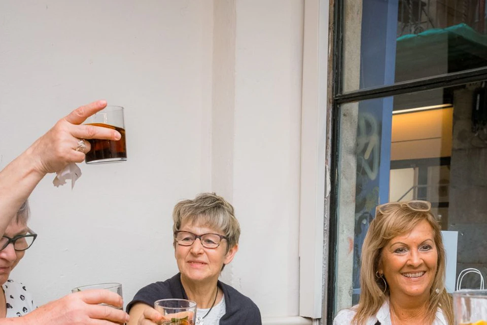 A group of people sitting at a table, smiling and toasting with drinks, with plates of food in front of them.