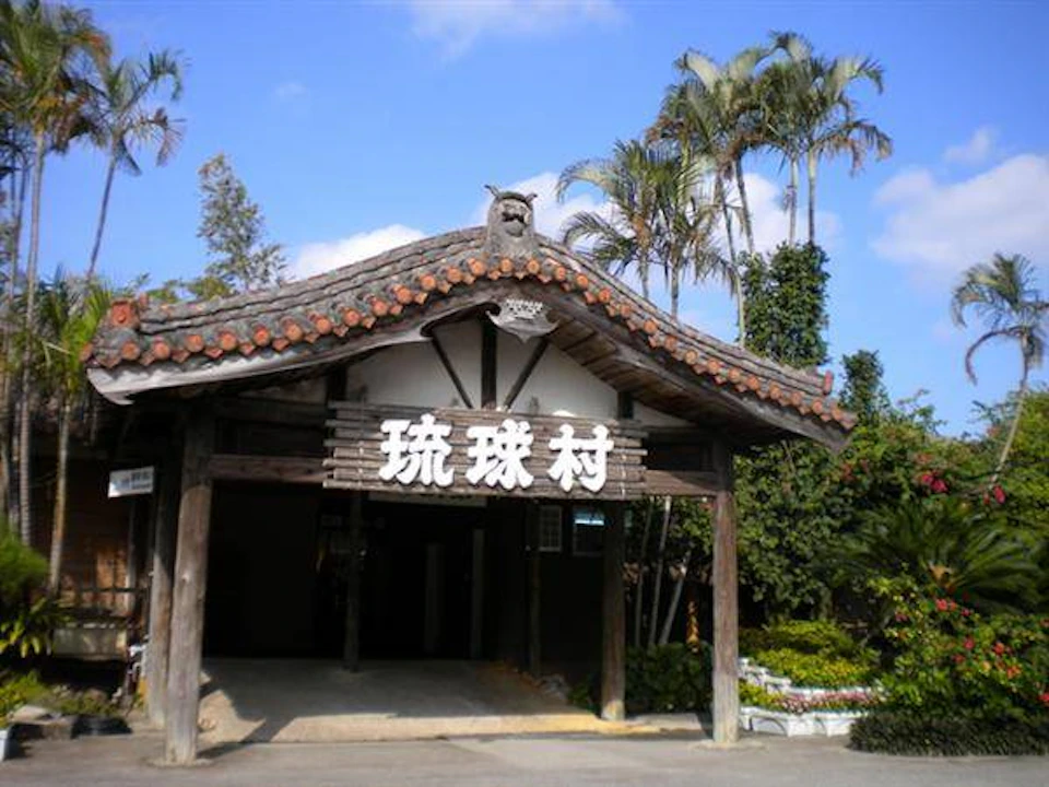 Traditional wooden gate with Japanese characters under a tiled roof, surrounded by trees on a sunny day.