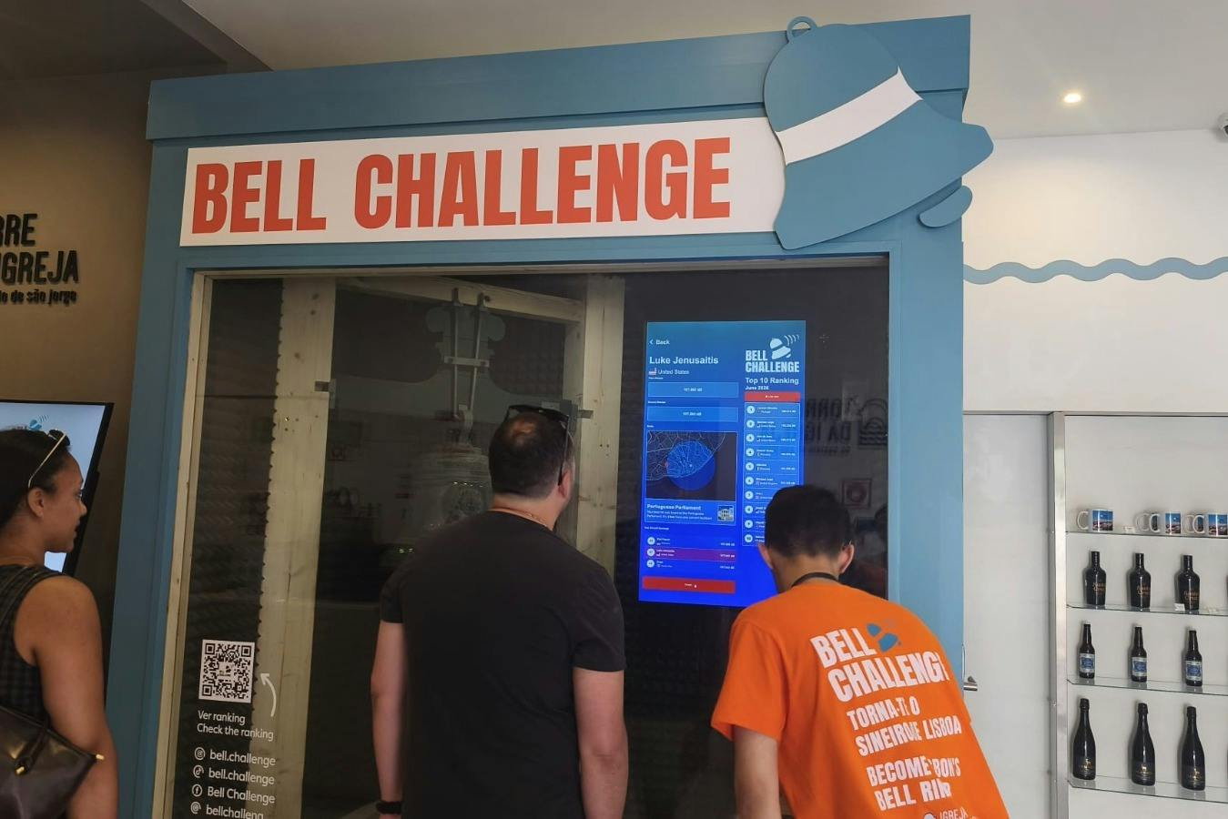 People observing a display labeled "Bell Challenge" with a screen showing rankings and information.