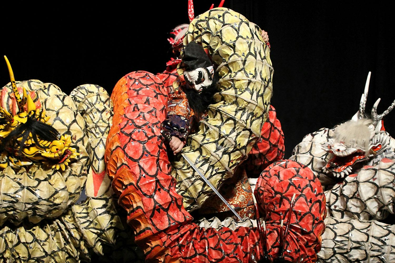 A person in ornate costume performing with large, colorful, snake-like structures in a theatrical setting.