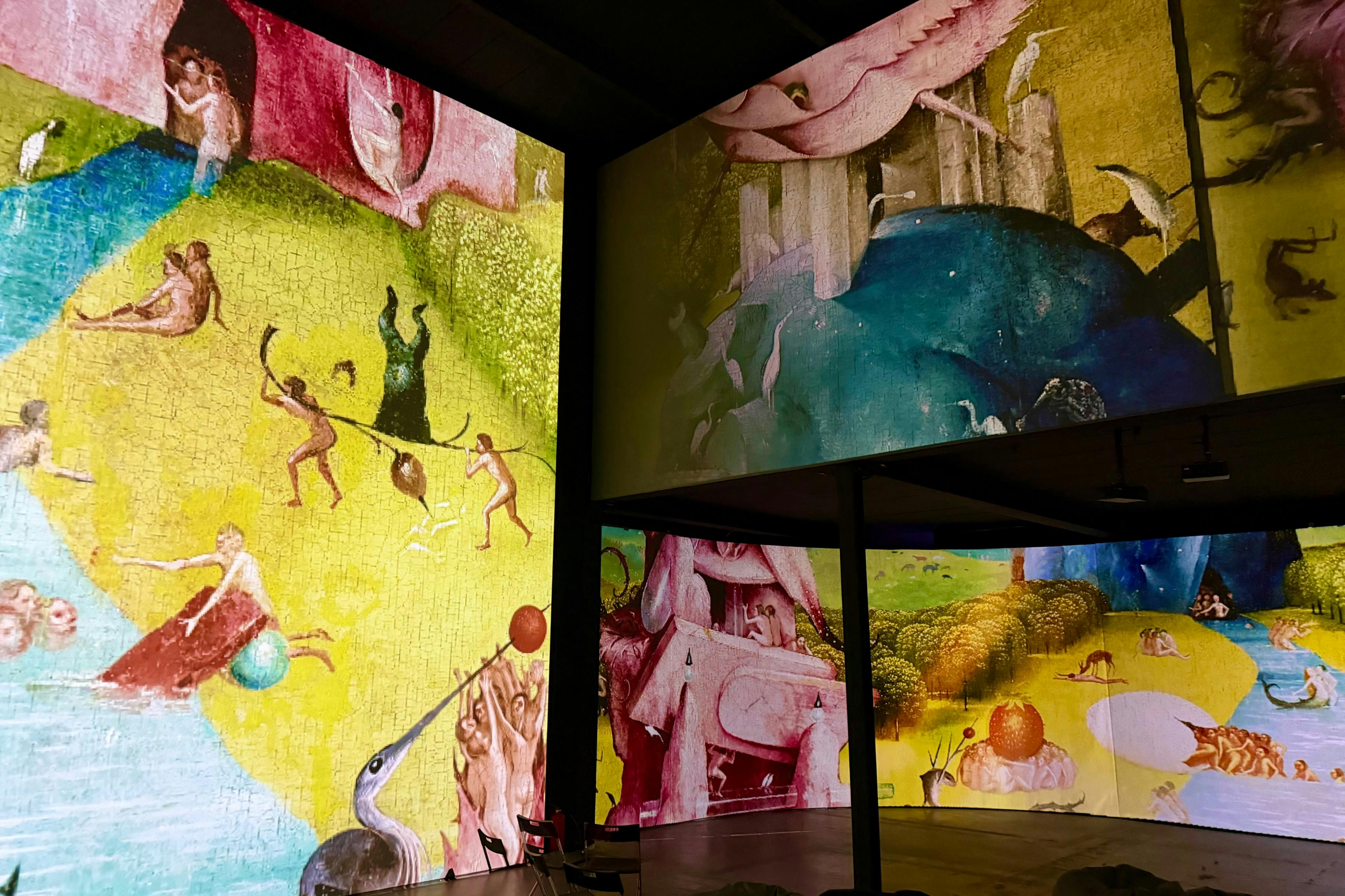 Projicering av ett surrealistiskt konstverk med många figurer, djur och abstrakta scener på stora omgivande skärmar.