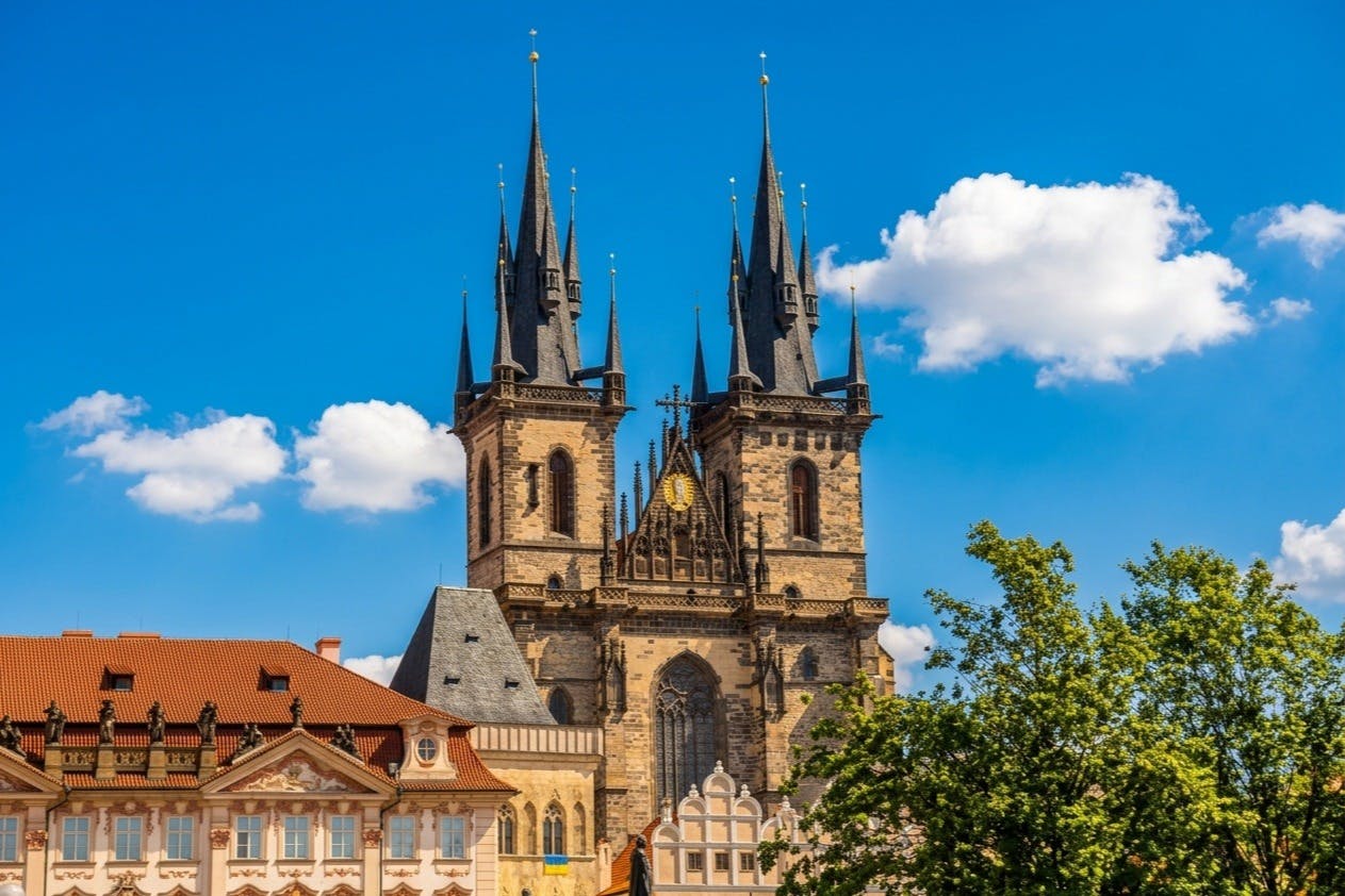 伝統的なヨーロッパの建物や木々に囲まれた、青い空の下に高い尖塔があるゴシック様式の大聖堂。