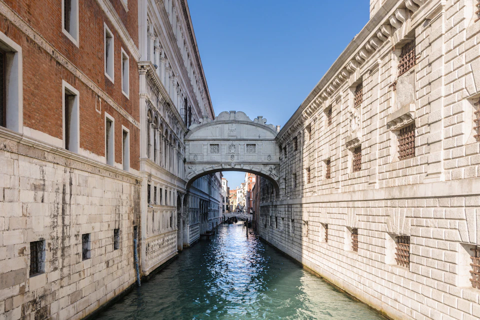 A canal in Venice flanked by historic buildings, with the ornate Bridge of Sighs connecting the buildings above the water.