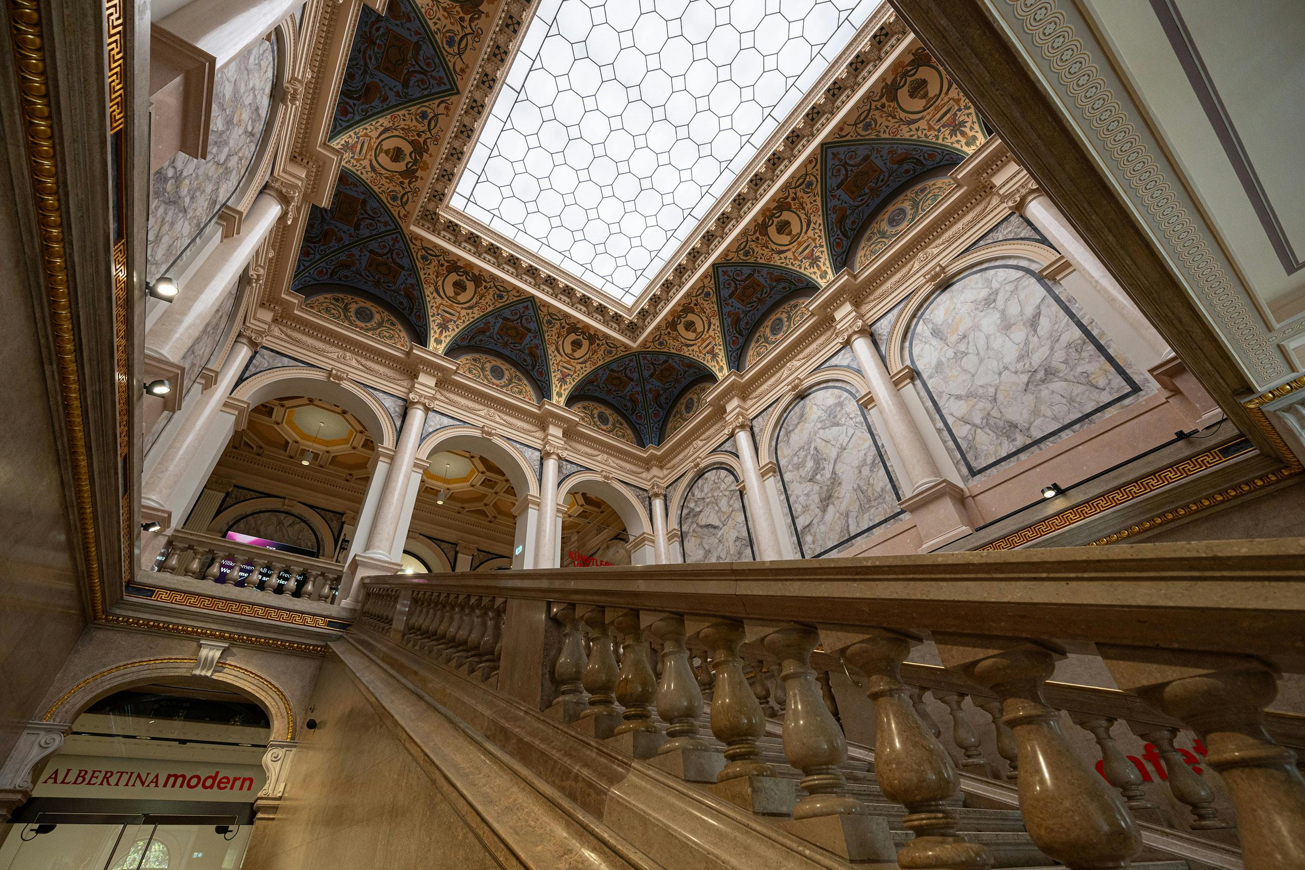 Περίτεχνη εσωτερική σκάλα με μαρμάρινα κάγκελα, θολωτή οροφή με περίπλοκα σχέδια και μεγάλο φεγγίτη που επιτρέπει το φυσικό φως.