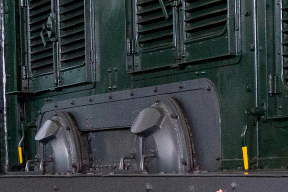 A woman with three children explore an old green train in a museum. One child climbs steps, and another points at the train.