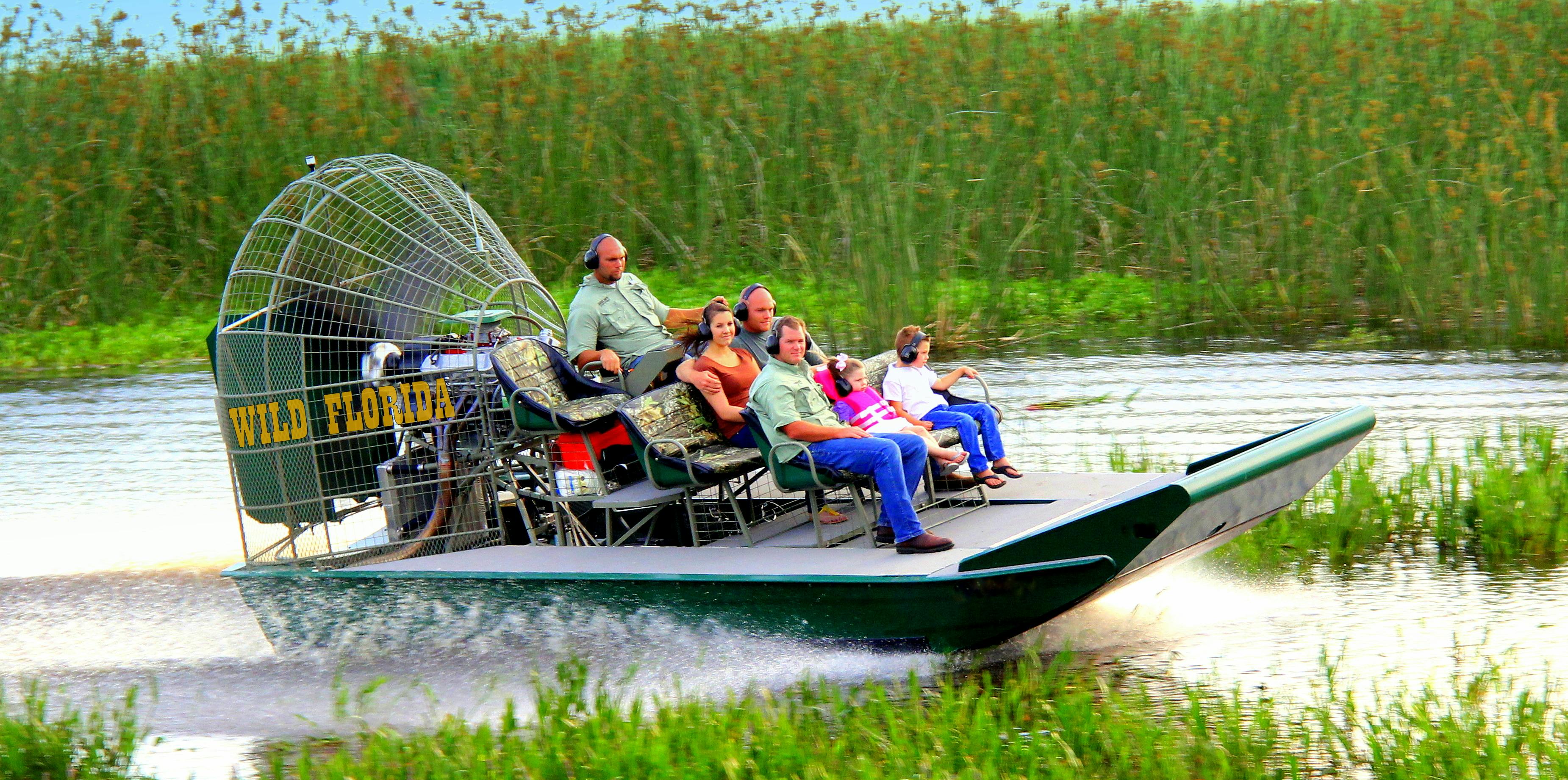 People wearing headsets riding an airboat labeled "Wild Florida" through tall marshy grass.