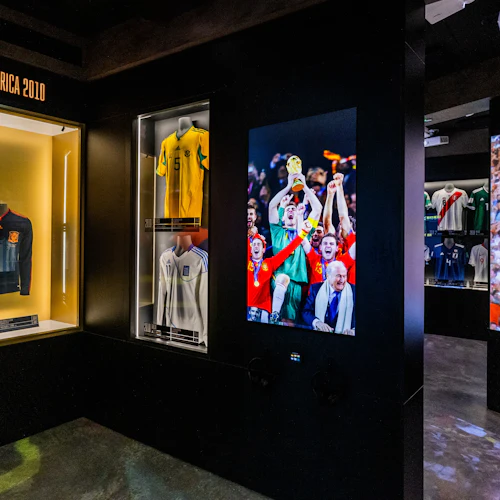 Visar fotbollströjor från olika lag och epoker med en bild av spelare som firar en seger, märkt "Sudáfrica 2010".