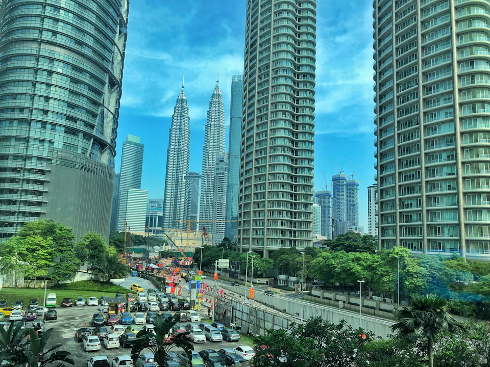 Cityscape with tall skyscrapers, including the Petronas Twin Towers in the background, and a busy street with traffic and construction.
