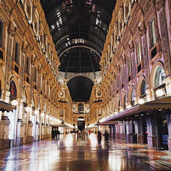 En utsmyckad, väl upplyst galleria med välvda butiksfronter, ett välvt tak i glas och reflekterande marmorgolv på natten.