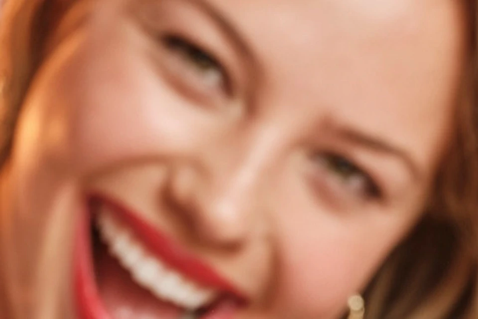 A smiling person holding two stacked burgers with cheese, lettuce, and meat patties in a restaurant setting.