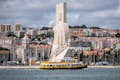 Barco amarelo navegando em frente ao Monumento aos Descobrimentos de Lisboa ao pôr do sol, capturando o histórico e cênico Rio Tejo