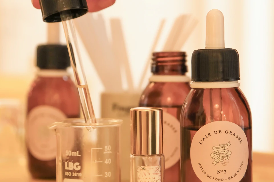A close-up of perfume-making tools, including droppers, beakers, and labeled bottles, arranged on a surface.