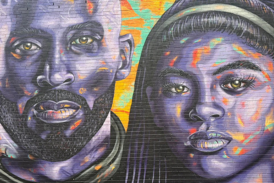 Colorful mural on a brick wall featuring two vibrant, purple-toned faces against an abstract, multicolored background.