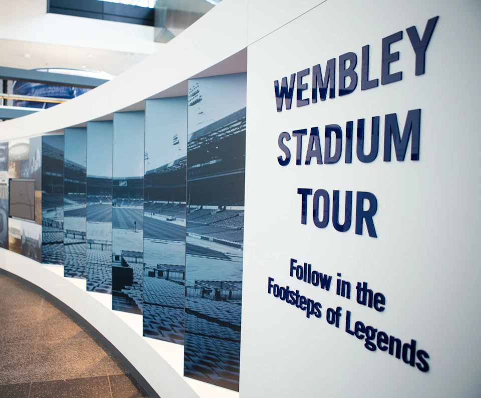 Panel display with images of Wembley Stadium and large text reading "Wembley Stadium Tour: Follow in the Footsteps of Legends."