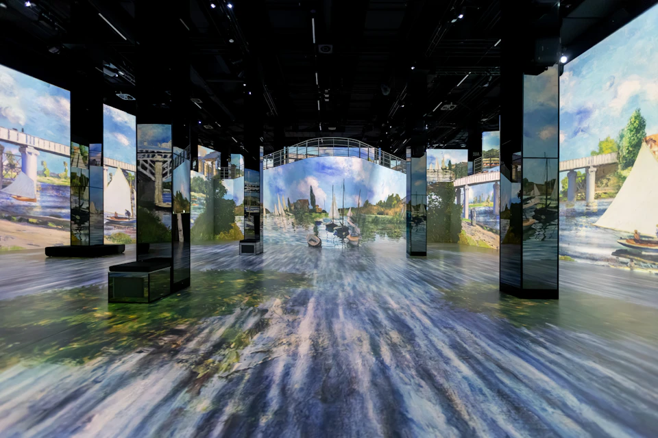 Immersive art exhibit with projected landscapes, water reflections, and boats displayed on walls and floor.
