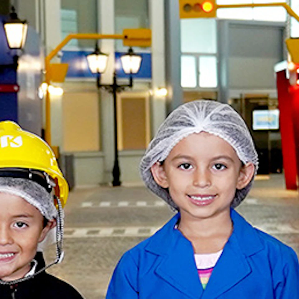 Six children dressed in various professional costumes, such as a firefighter, doctor, and chef, stand on a crosswalk in a themed setting.