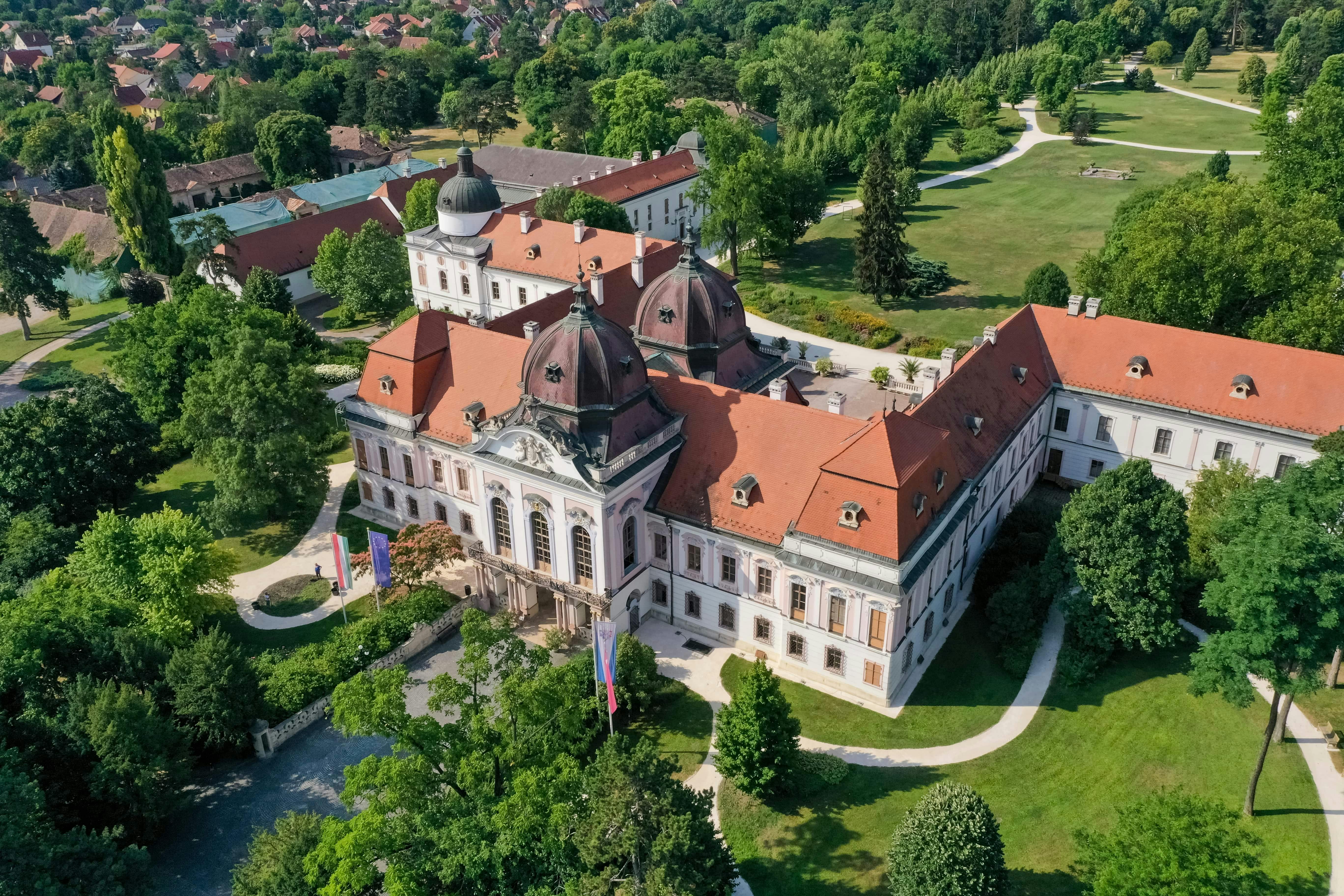 울창한 녹지와 산책로로 둘러싸인 빨간색 타일 지붕이 있는 크고 화려한 건물의 공중 전망.
