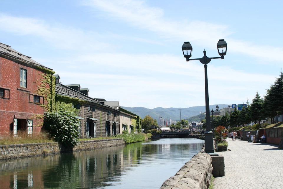 A canal lined with stone buildings covered in greenery, a lamp post, and a clear blue sky in the background.