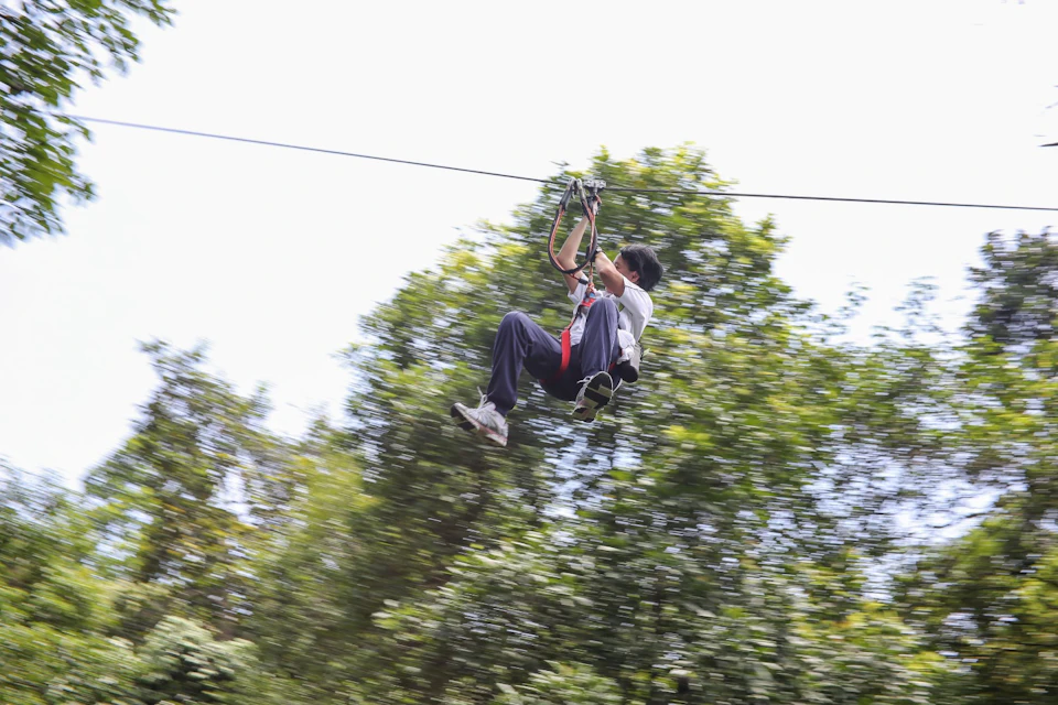 A person ziplining through a forested area, holding onto the harness, with trees blurred in the background.
