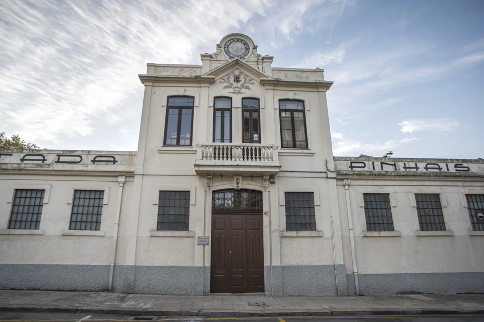 A white historical building with large windows and a decorative facade under a blue sky with clouds.