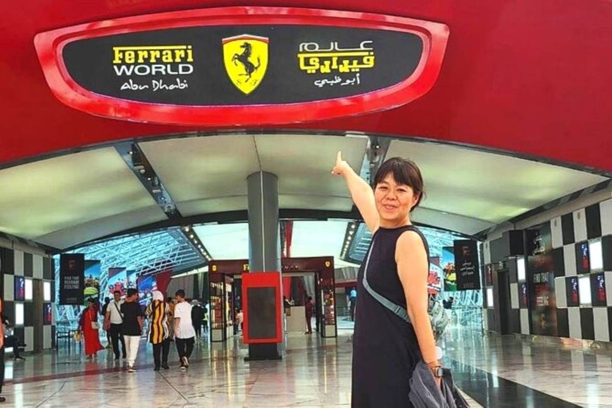 赤と白の装飾が施されたモダンな屋内エリアで、フェラーリワールドの看板を指差している女性。