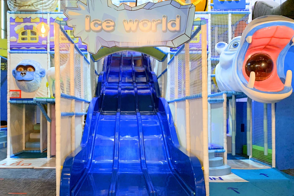 A blue slide in a colorful indoor play area with a sign reading "Ice World" above the slide.