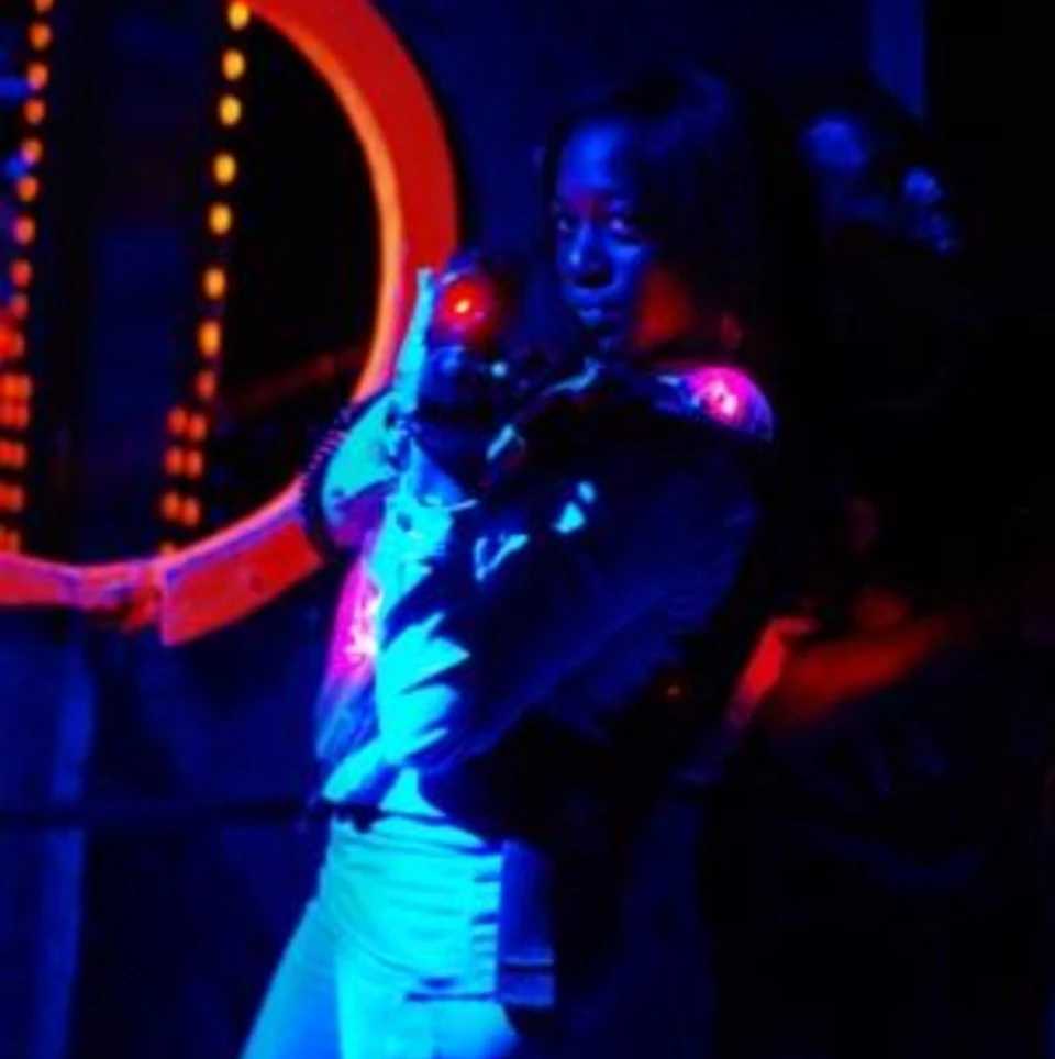 Person wearing glowing gear aiming a laser tag gun in a dark, neon-lit arena.