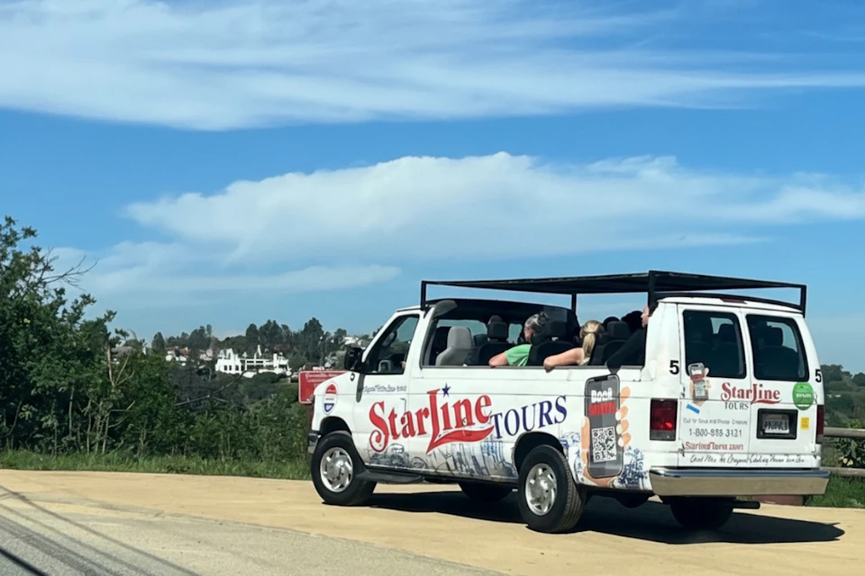 An open-top tour van labeled 'Starline Tours' parked on a roadside, with passengers seated and scenery in the background.