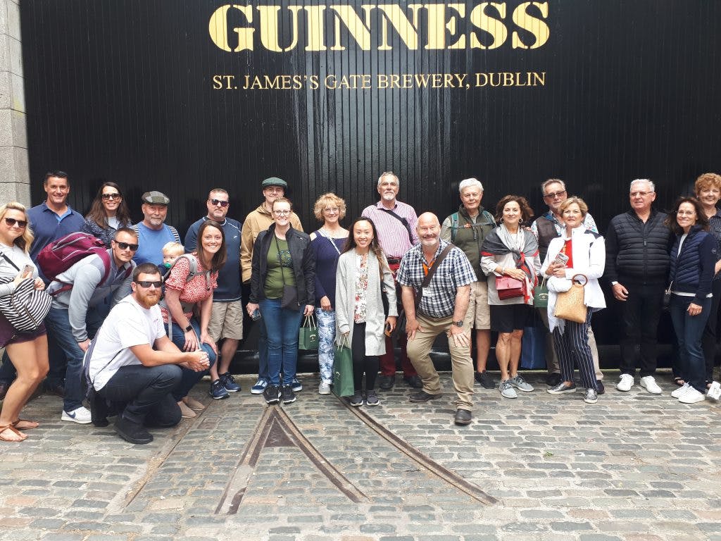 Gruppo di persone in posa davanti all'ingresso della fabbrica di birra Guinness St. James's Gate, Dublino.